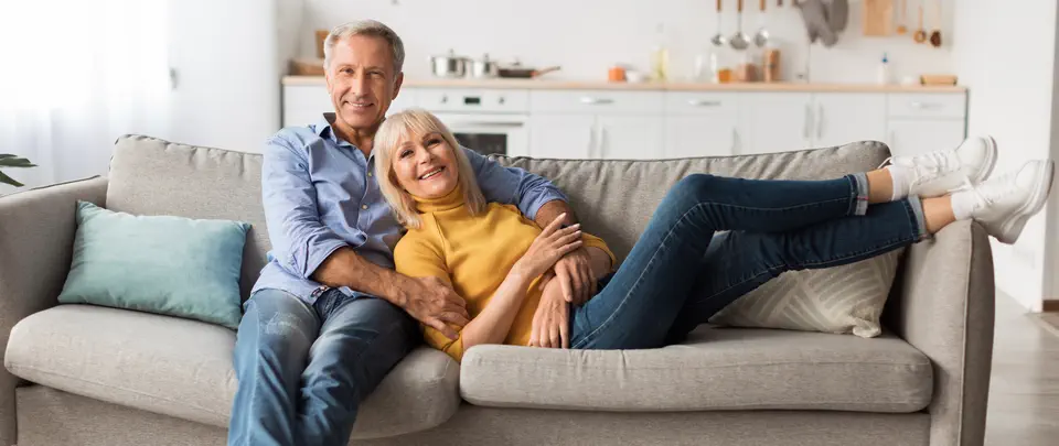 Ein Bestager-Paar sitzt entspannt auf einer Couch