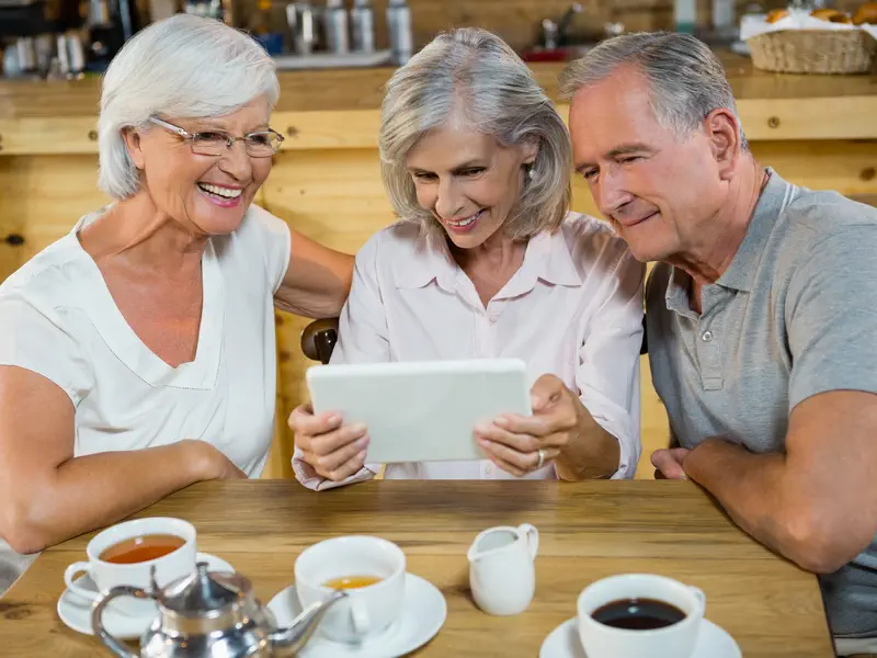 Drei Best Ager schauen auf ein Tablet beim Frühstück