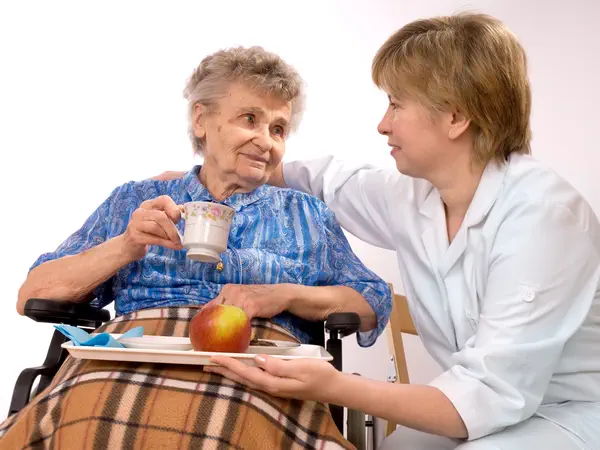Eine Pflegerin legt ihre Hand um eine ältere Frau, die Tee trinkt