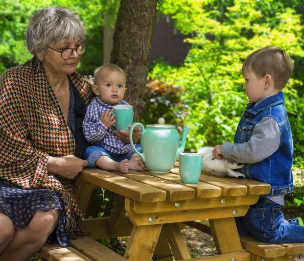 Oma sitzt mit zwei Enkeln an einem Holztisch im Wald