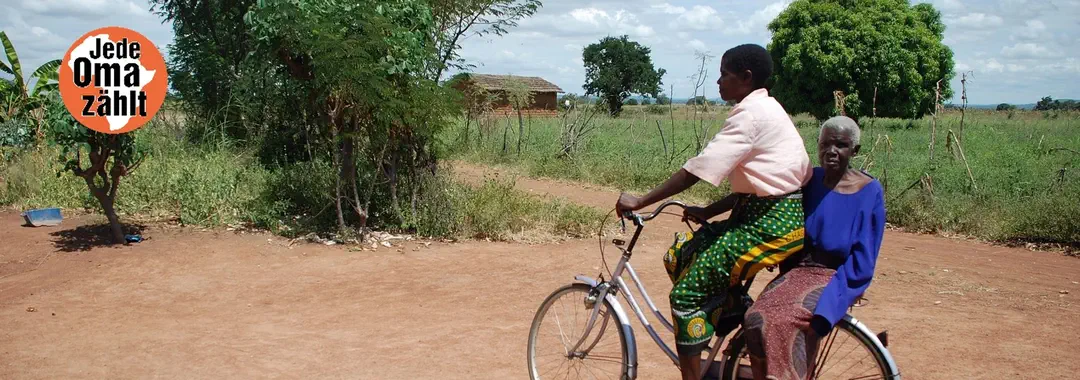 Hier sehen Sie das Titelbild der HelpAge-Kampagne "Jede Oma zählt" – eine afrikanische Oma auf dem Fahrrad in einem Dorf.