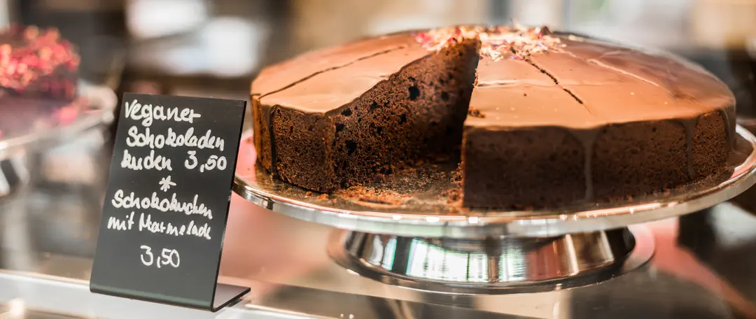 Ein veganer Schokoladenkuchen mit einem Preisschild in der Vitrine beim Kuchentratsch.
