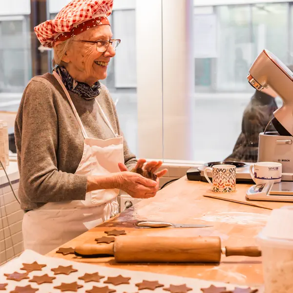 Eine ältere Mitarbeiterin von Kuchentratsch formt Plätzchen und lacht dabei.