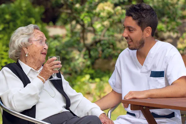 Symbolfoto: Ein Pfleger unterhält sich mit einer älteren Dame im Garten