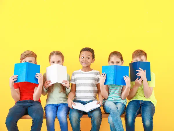 Symbolfoto: Kinder beim Lesen auf einer Bank sitzend